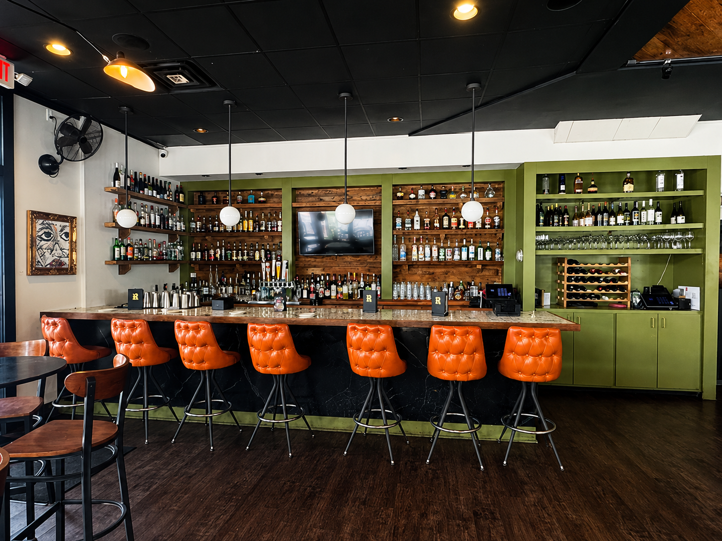 Wide view of POUR's bar with orange stools and green accent wall